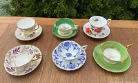 Top view of all 6 cups and saucers arranged on wooden table, showing patterns and overall style.