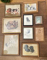Overview photo of nine framed dog pictures laid out on a table including various breeds and styles.