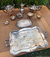 Photo showing full set arranged on wooden surface with coffee pot, teapot, creamer, covered sugar bowl, two open sugar dishes, two trays, and small round containers.