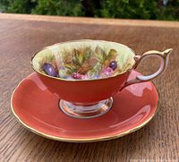 Front view of Aynsley teacup and saucer set showing coral exterior and gold trim