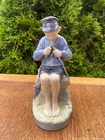 Front view of Royal Copenhagen porcelain figurine of boy mending net, showing detailed painting and pose.