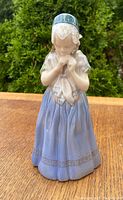 Front view of the Royal Copenhagen porcelain girl figurine with blue skirt and headscarf, hands near chest.