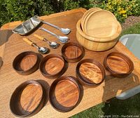 Wooden salad bowls in varied sizes and tones arranged on wooden table with metal and wood-handled serving utensils.