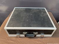 Closed black aluminum-framed carrying case with two metal latches and handle, approx. 20 inches long.