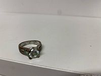 Front angled view of silver-tone ring with clear round stone showing tarnishing and wear.