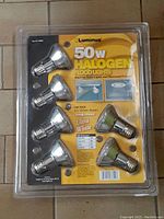 Photo of sealed package containing six Luminus 50W halogen flood light bulbs on tiled floor.