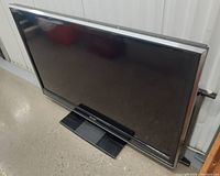 Full view of the 52-inch Sharp Aquos LCD TV with stand, showing the screen and frame.