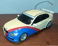 Front and side view of BMW Motorsport toy car showing white body with blue and red stripes, BMW and Castrol decals, antenna wire and detailed wheels.