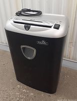 Front and side view of Fellowes OS12Cs shredder showing black bin, silver top with control switch, power cord coiled on top, and clear plastic window.