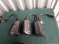 Three black wireless remote control outlet receivers with power plugs and switches on a green surface.