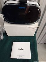 Front view of the HooToo VR headset placed on top of its white packaging box with user guide booklet in front.