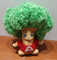 Plush doll mascot with a dark green textured afro and red shirt with white 'A'