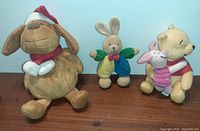 Front view of three plush dolls - dog with Santa hat, bunny with bow tie, and Winnie the Pooh with Piglet