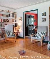 Two Ikea Poang chairs with light-colored covers arranged in a bright living room with wood flooring and bookshelves.