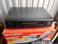 Front view of Sharp VC-H800U VHS video cassette recorder placed on original orange box with branding and model information visible.