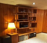 Bookshelf against wood-paneled wall with warm lighting, showing modular cube elements and vertical supports, some electronic items placed on shelves.