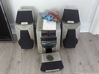 Front view of Sony MHC-F150 mini hi-fi system including the main receiver, CD changer, cassette players, five speakers, remote control, user manual, and speaker cables.