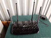 Front and top view of the black TP-Link Archer A6 wireless router showing four external antennas and textured surface.