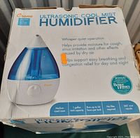 Front view of original product box showing Crane branding, product name, and features such as whisper quiet operation, 1 gallon tank capacity, 24-hour run time, no filter required, 360° mist nozzle, and medium sized room suitability.