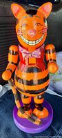 Front view showing detailed colorful hand painted orange and black wooden cat figure with a big grin and purple bow tie.