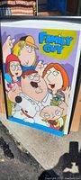 Framed Family Guy poster showing main characters and logo, placed outdoors on concrete floor.