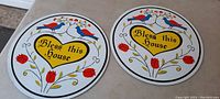 Two round hex signs on hardboard each 14 inches in diameter with colorful painted folk-art style motifs, including birds and flowers, and text 'Bless this House' in a heart at center.