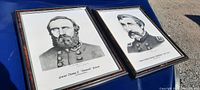 Photo of both framed prints featuring military officers Stonewall Jackson and Joshua Chamberlain placed side by side outdoors on a blue surface.