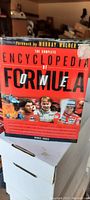 Front cover of the hardcover book titled 'The Complete Encyclopedia of Formula 1' with images of famous drivers and foreword by Murray Walker.