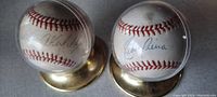 Two vintage autographed baseballs in clear protective display cases with brass bases, shown side by side.