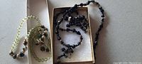 Two necklaces visible: one green bead string necklace and one black bead necklace with gold accents, shown partially inside a box and on a surface.