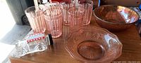 Photo of six pink/orange Depression glass drinking glasses with vertical ridge pattern and two pressed glass bowls. Also includes a small clear glass bottle with a red label.