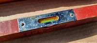 Close-up of metal level bubble encased in metal frame on red painted wooden level tool.