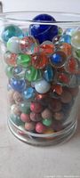 Clear glass jar filled with colorful antique marbles showing variety of colors and sizes including a large cobalt blue marble at the top