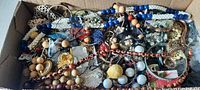 Box flat with a variety of mixed costume jewelry including necklaces, bangles, and bracelets showing the range of colors and materials.