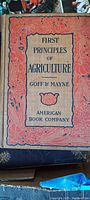 Photo of the book cover showing the title 'First Principles of Agriculture' by Goff & Mayne, published by American Book Company with decorative red and beige design