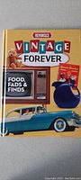 Cover of the 'Reminisce Vintage Forever: Food, Fads & Finds' book showing a yellow background with retro-themed images including a classic car and TV set.