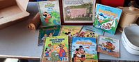 Photo of nine vintage Little Golden Books arranged on a table with visible titles and a framed nursery rhyme picture behind them.