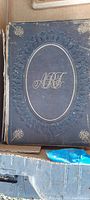 Front cover of the hardcover book showing embossed decoration, gold monogram initials, dark leather with wear and loose binding