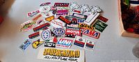 Photo showing a large assortment of vintage motorcycle racing stickers spread out on a table, including logos from Motul, AMA, AAA, AGV, and Michelin Man.