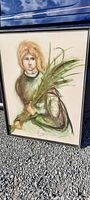 Framed watercolor painting showing a young girl holding green plants, in a simple black frame, resting on gravel.