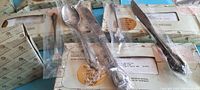 Photo showing multiple boxed sets of individually wrapped stainless steel flatware pieces including knives, forks, and spoons with decorative handles.