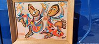 Frontal image of the painting showing two abstract dancing figures in colorful attire with a wooden frame.