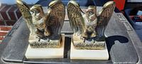 Pair of brass eagle bookends on marble bases seen from the front, showing bright detailed eagles and white bases with minor discoloration on one corner.