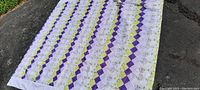 Quilted bedspread laid out flat outside, showing full size and diagonal color pattern in purple, green, and floral squares.