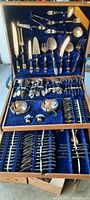 Open wooden case showing full goldtone flatware set with knives, forks, spoons, and serving utensils organized inside.