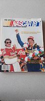 Front cover of the 1987 NASCAR Official Yearbook and Press Guide showing drivers in racing uniforms with colorful branding and celebration pose