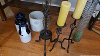 Four black metal candle holders each holding a yellow pillar candle. Three ceramic crocks, two light-colored and one dark blue with lid visible.