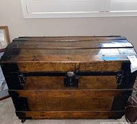 Full front view of vintage wooden chest with black metal corner metal and lock hardware.
