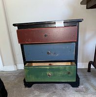 Front view of small wooden chest with three colored drawers red, blue and green, and black frame.