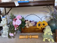Angel sculpture, faux flowers in wooden box, sunflowers, green ceramic turtle figurines, wooden spindle piece, and green vase with faux lavender visible under table.